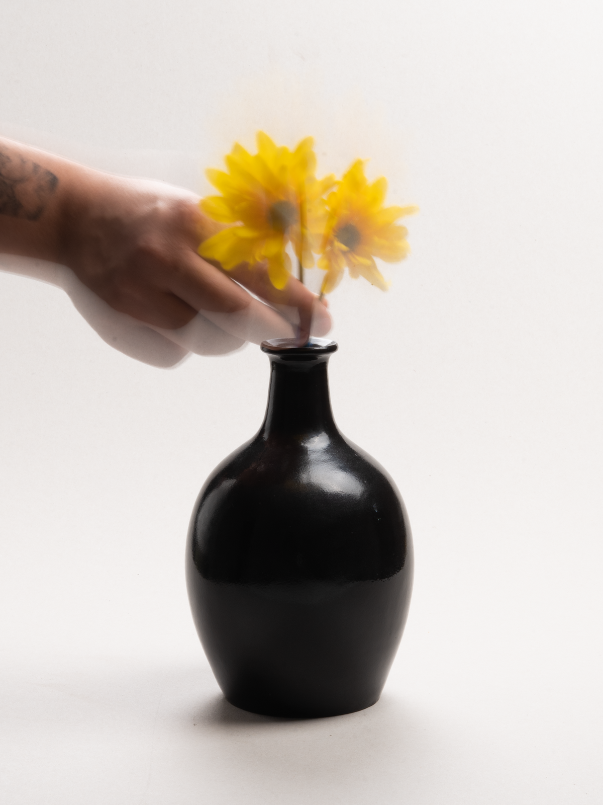 Una mano coloca flores amarillas en un florero negro de Uno Nueve
